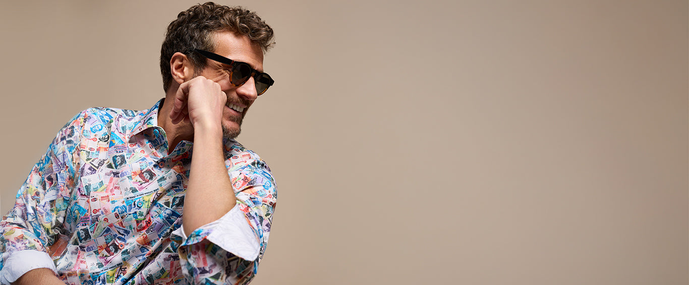 A smiling man wearing a brightly patterned shirt featuring international currency.