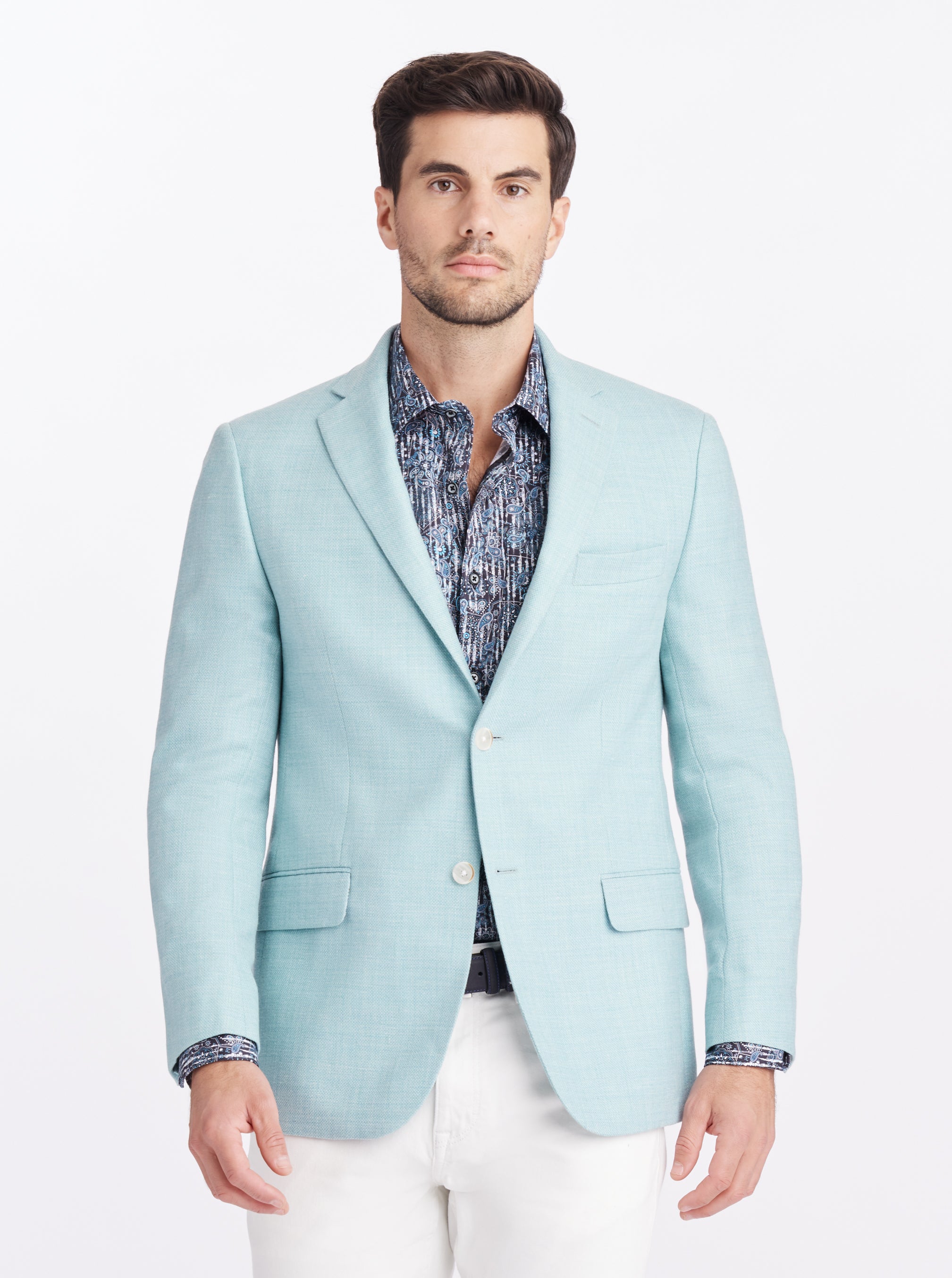 Man wearing a light blue blazer over a patterned shirt on a white background