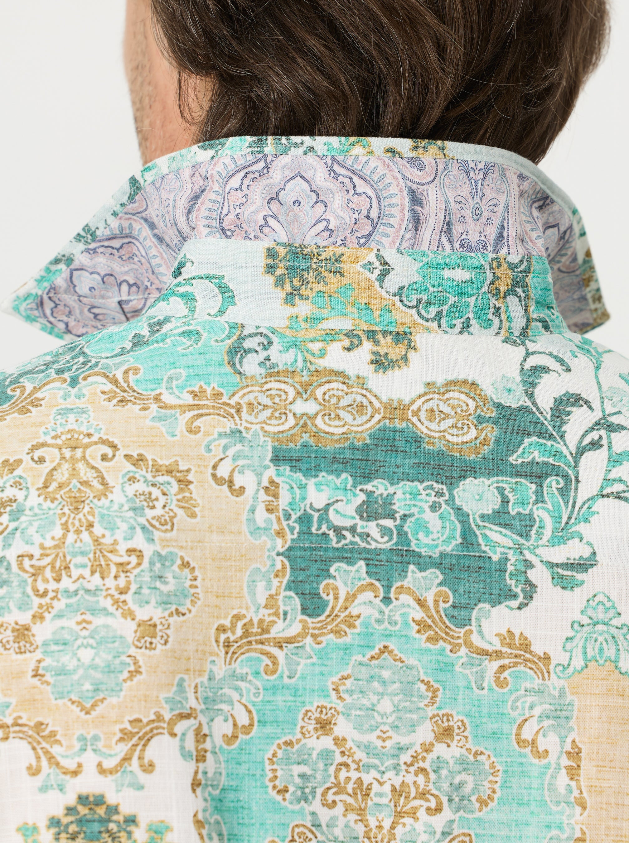 Close-up of a person wearing a ornamental medallions patterned shirt with a white background