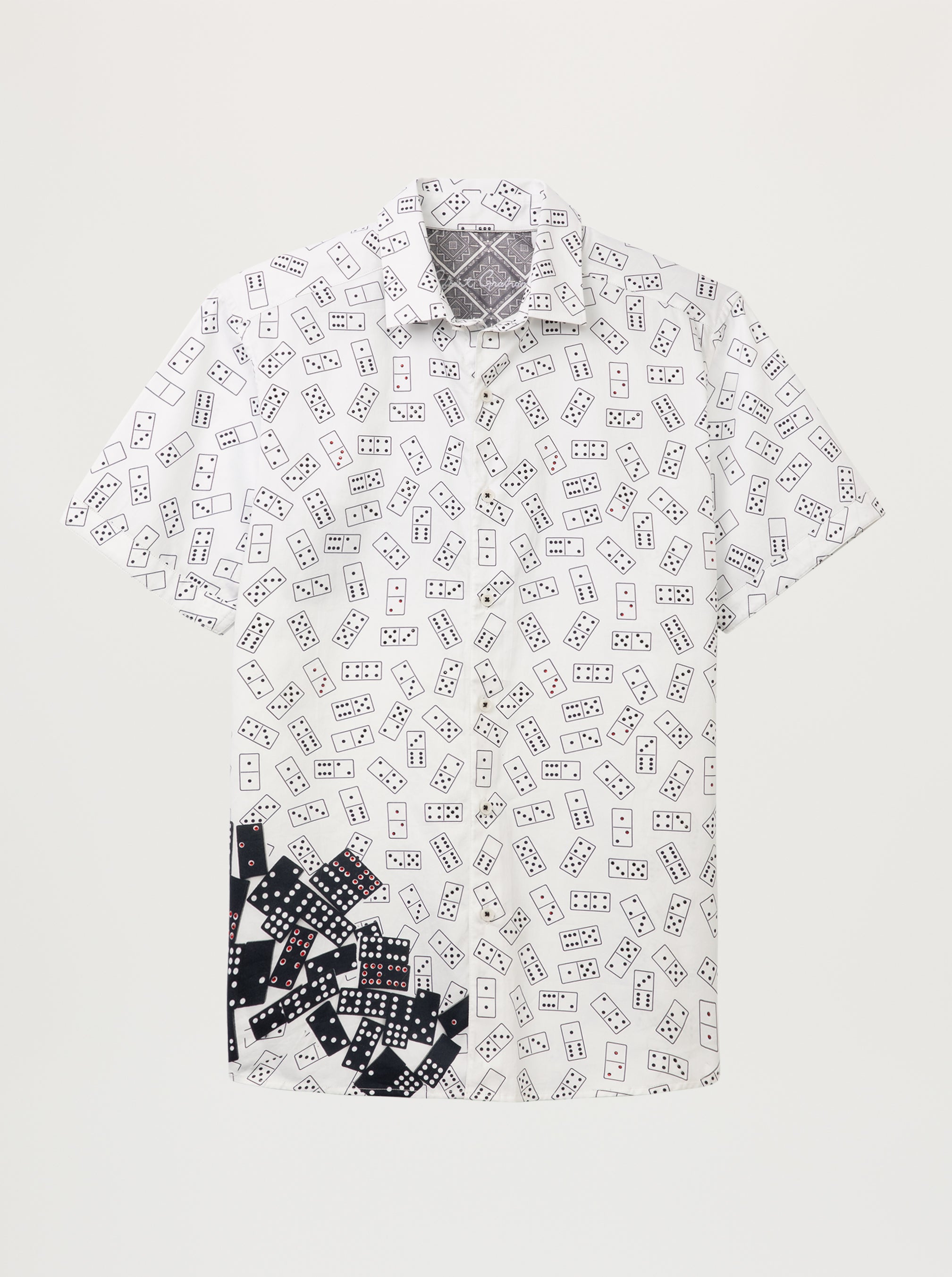 A short-sleeve button-up shirt with an all-over black domino pattern on a white base, featuring a solid black and white domino print cluster on the lower left side, displayed against a light gray background.