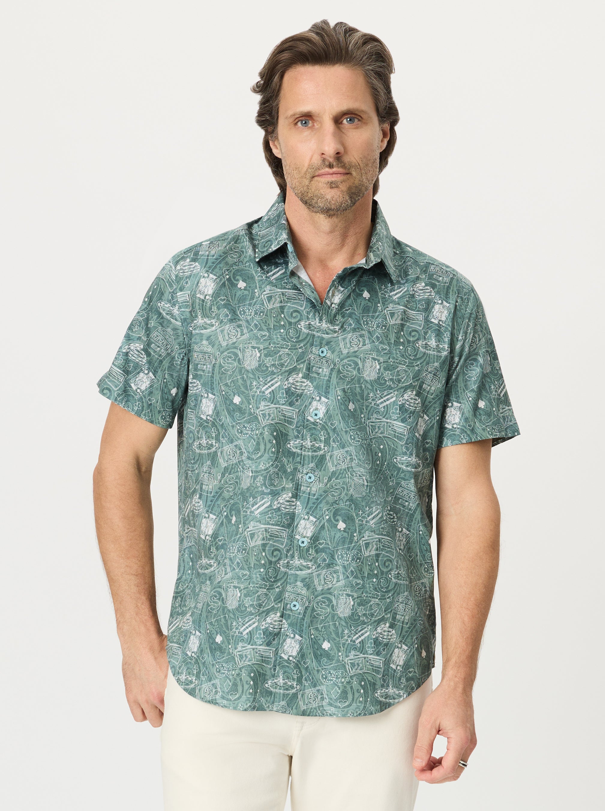 Man wearing a short-sleeve button-up shirt in sage green with a white casino line-art poker chips, playing cards, and slot machines, against a light gray background.