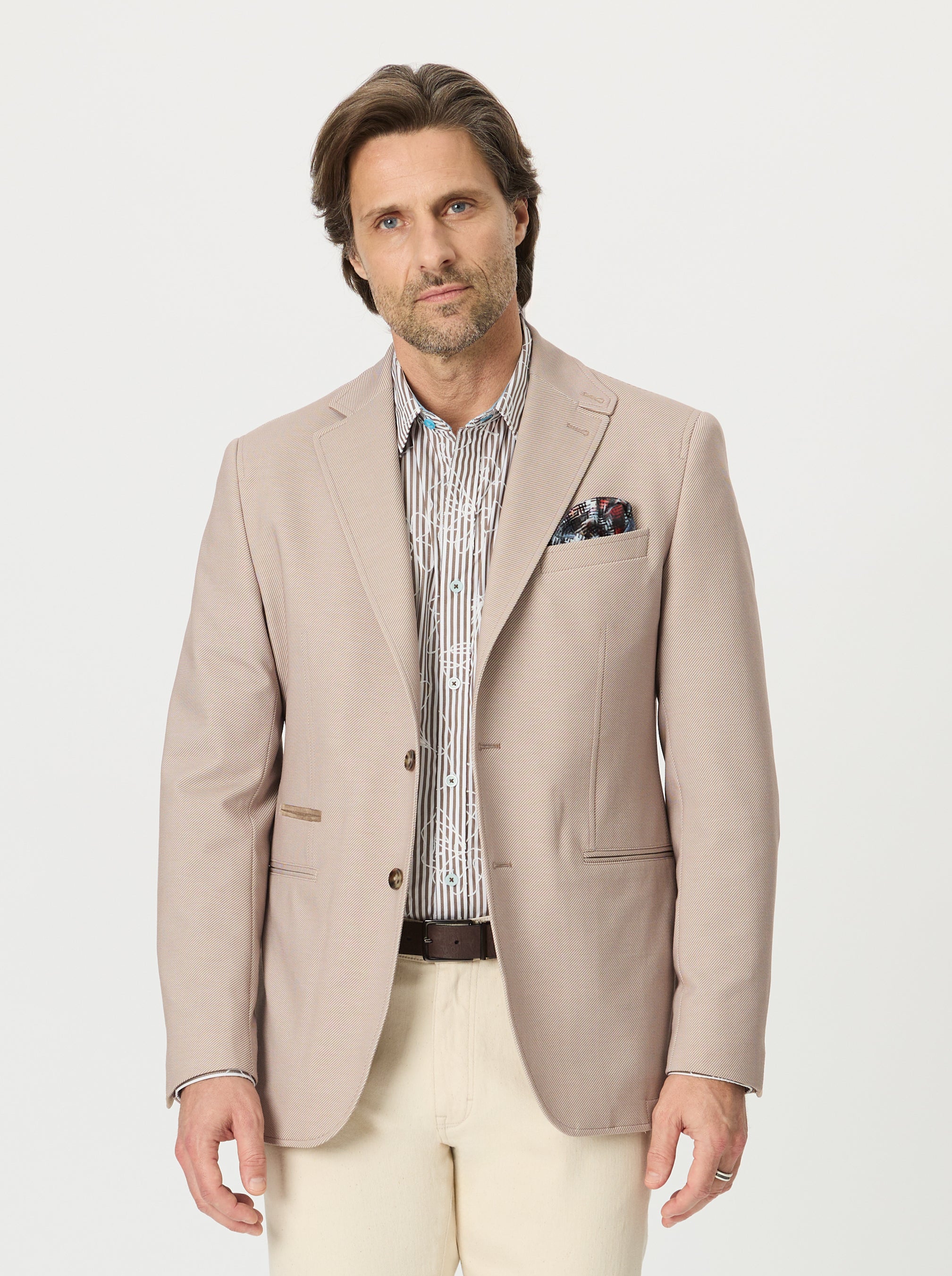 Man wearing a beige blazer over a patterned shirt with a white background