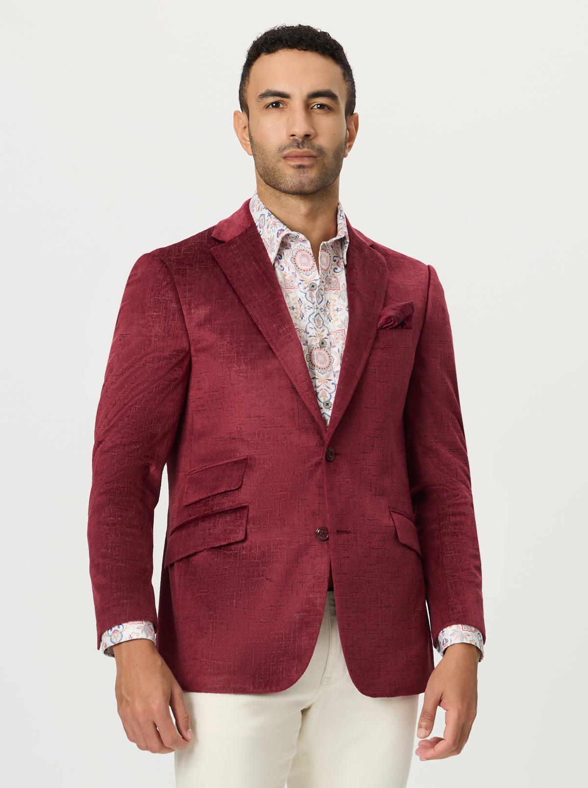 Man wearing a burgundy velvet blazer over a patterned shirt with a white background