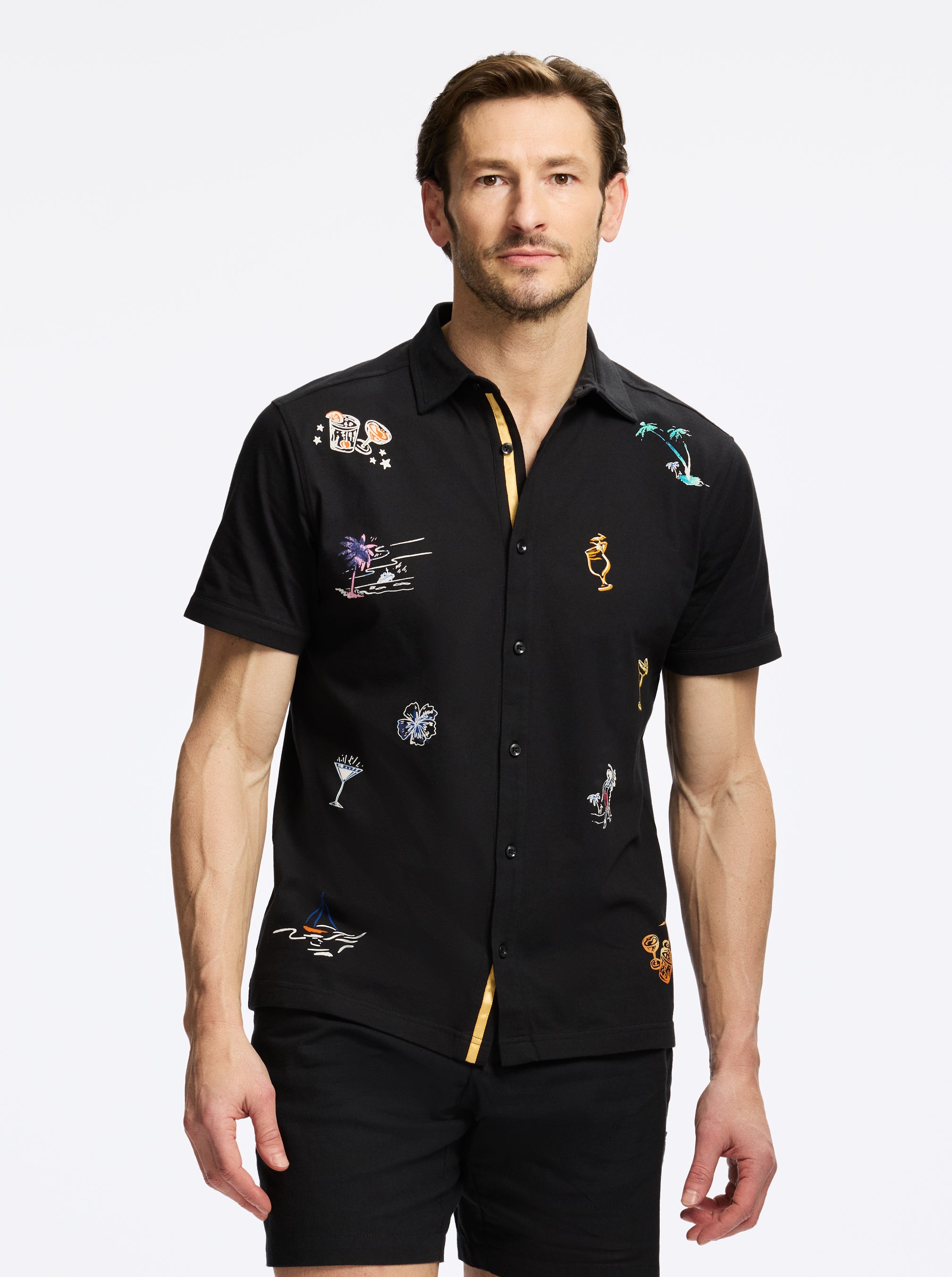 Man wearing a black shirt with colorful embroidered designs on a white background