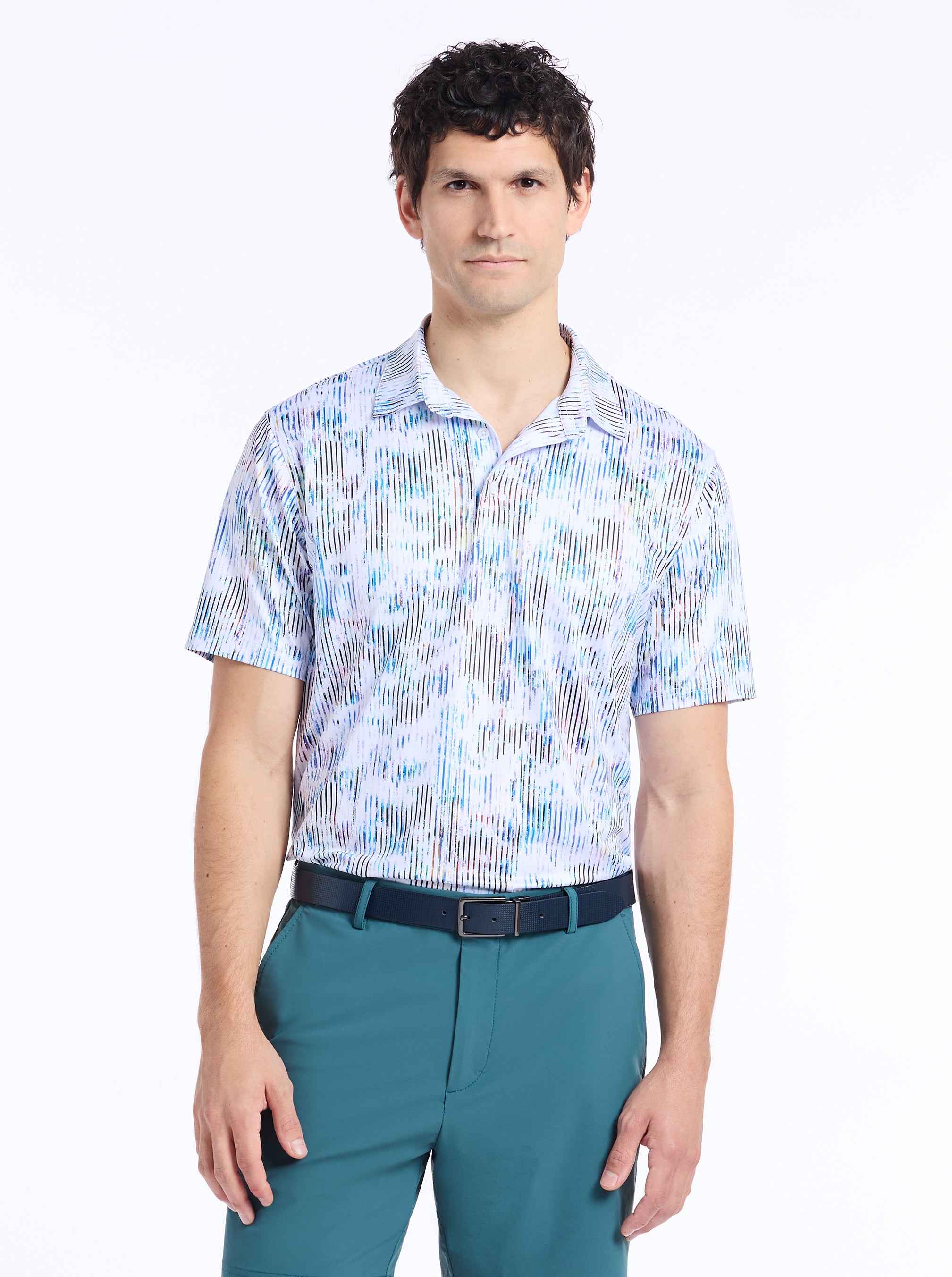Man wearing a patterned short-sleeve shirt and teal pants on a white background