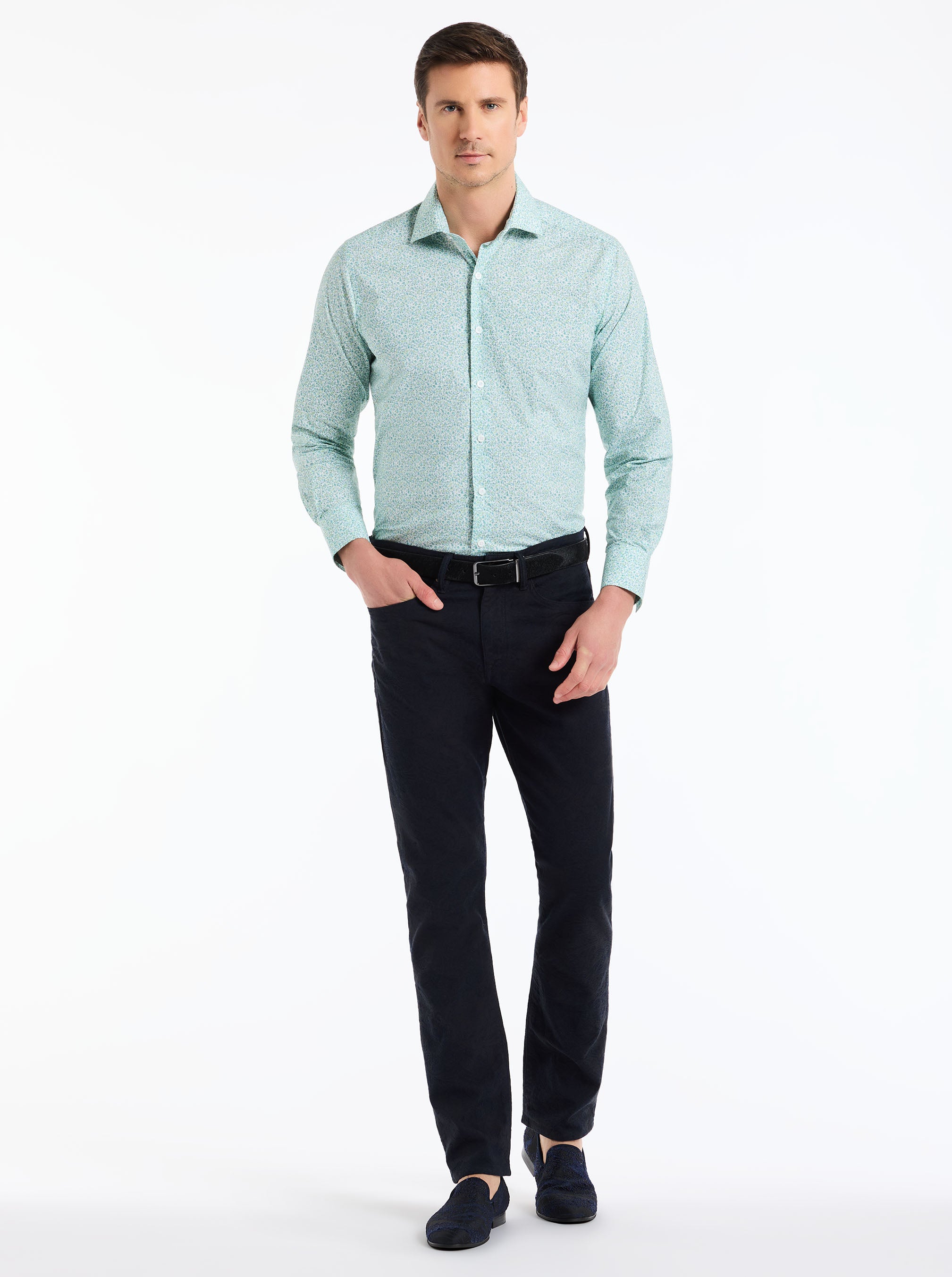 Man wearing a light green patterned shirt and black pants on a white background