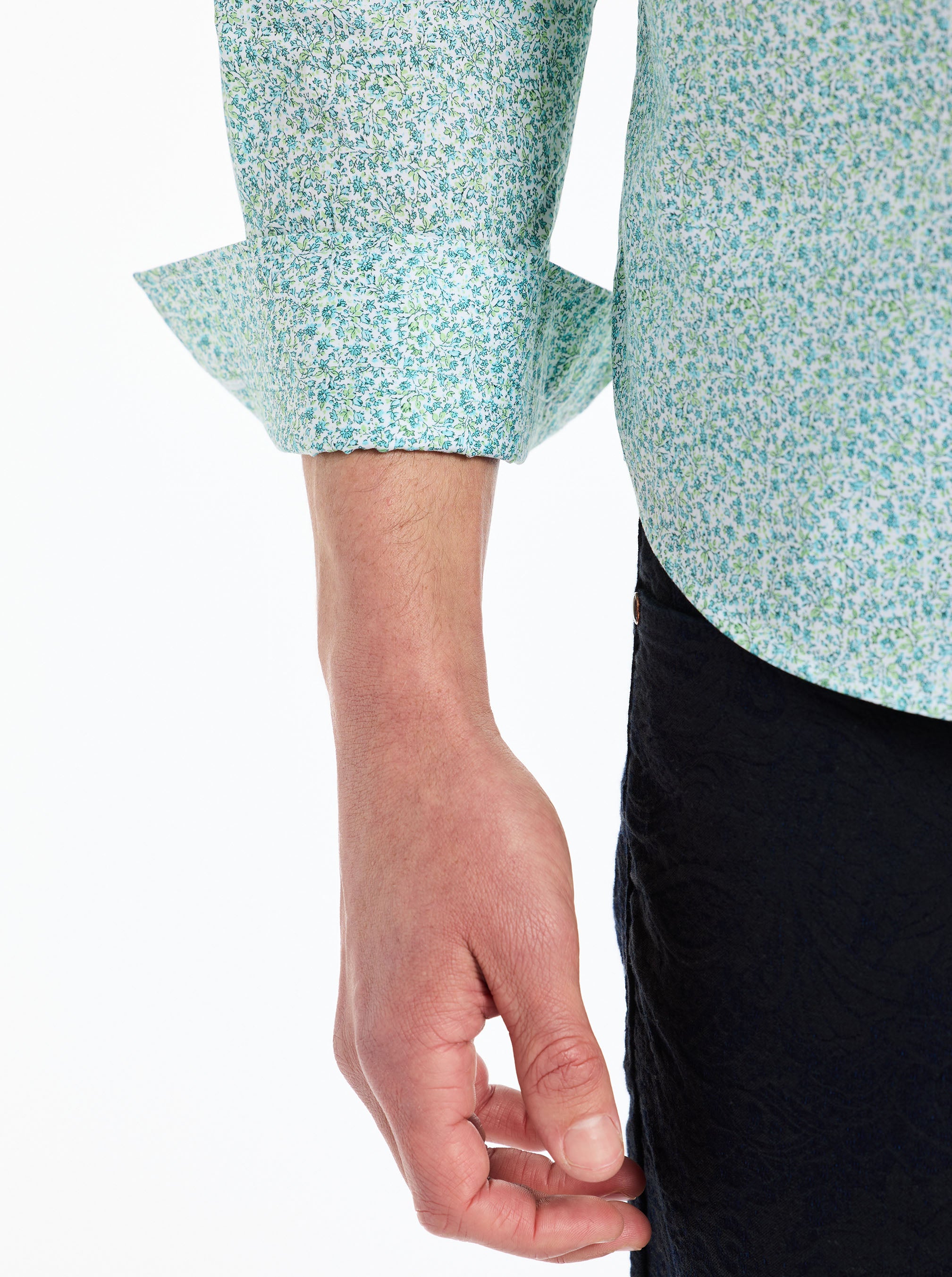 Close-up of a person wearing a light blue floral-patterned shirt with rolled-up sleeves on a white background.