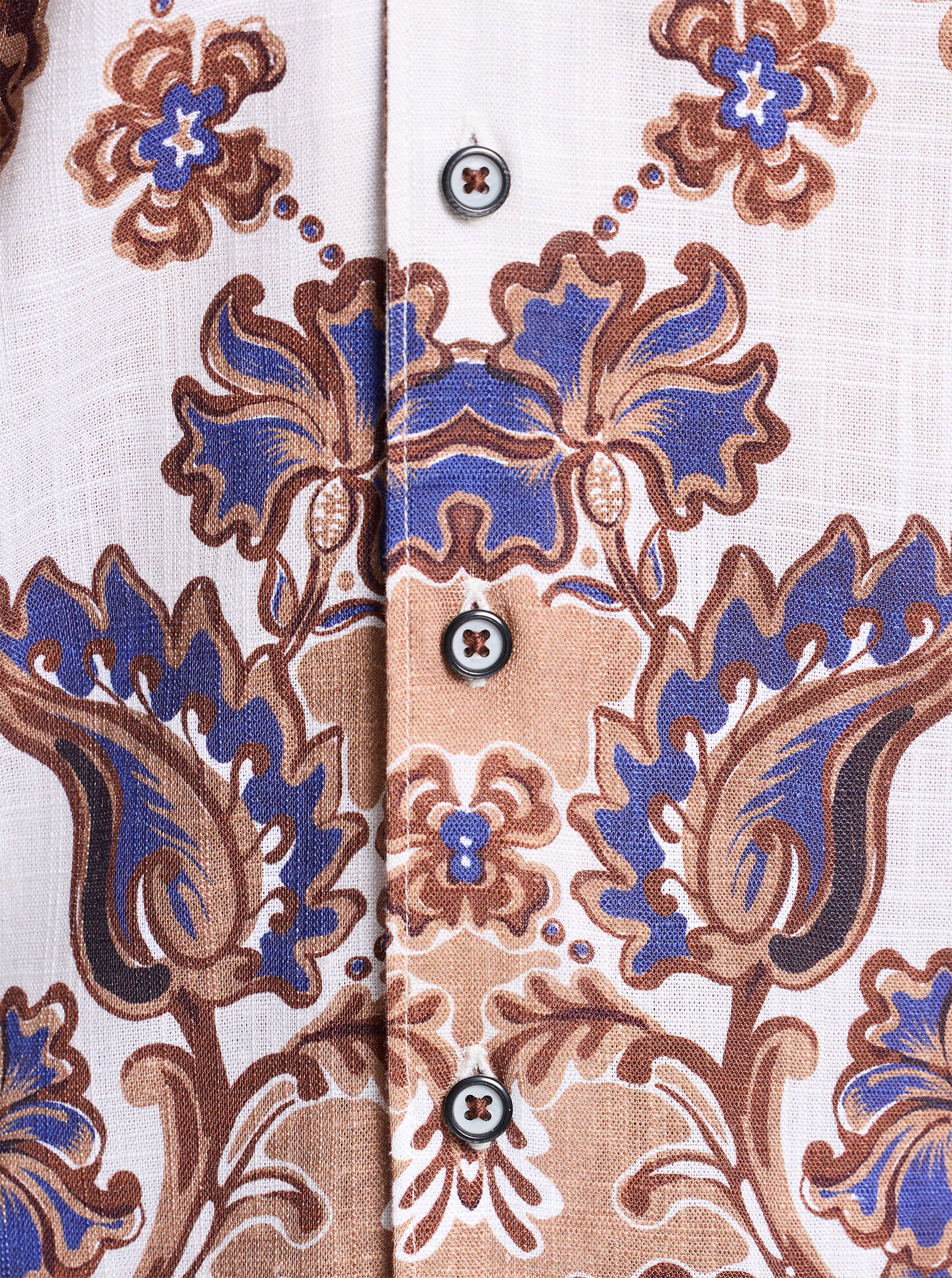 Close-up of a ornate patterned shirt with blue and brown floral design on a white background