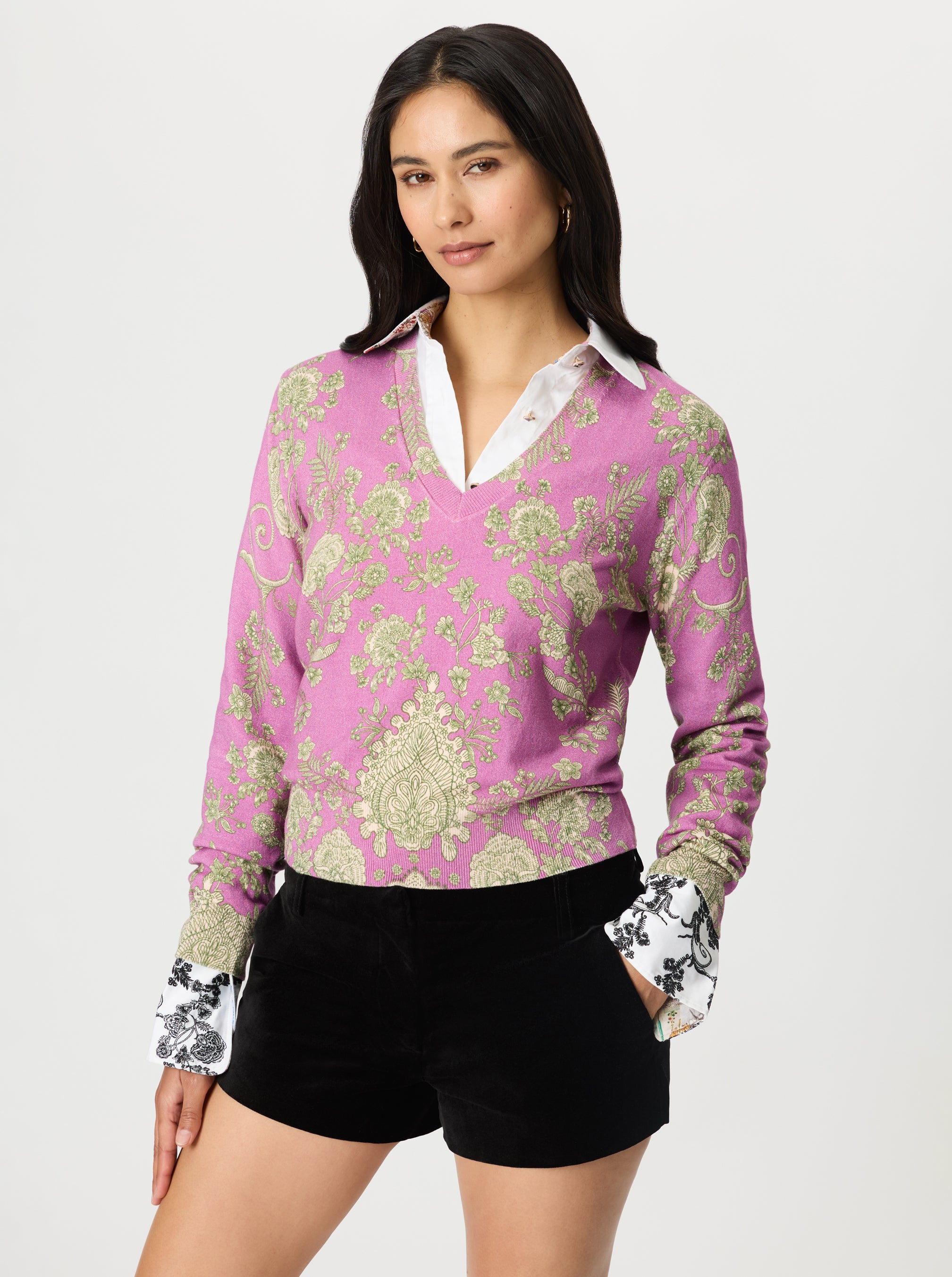 Woman wearing a pink patterned sweater with a white shirt underneath on a light gray background