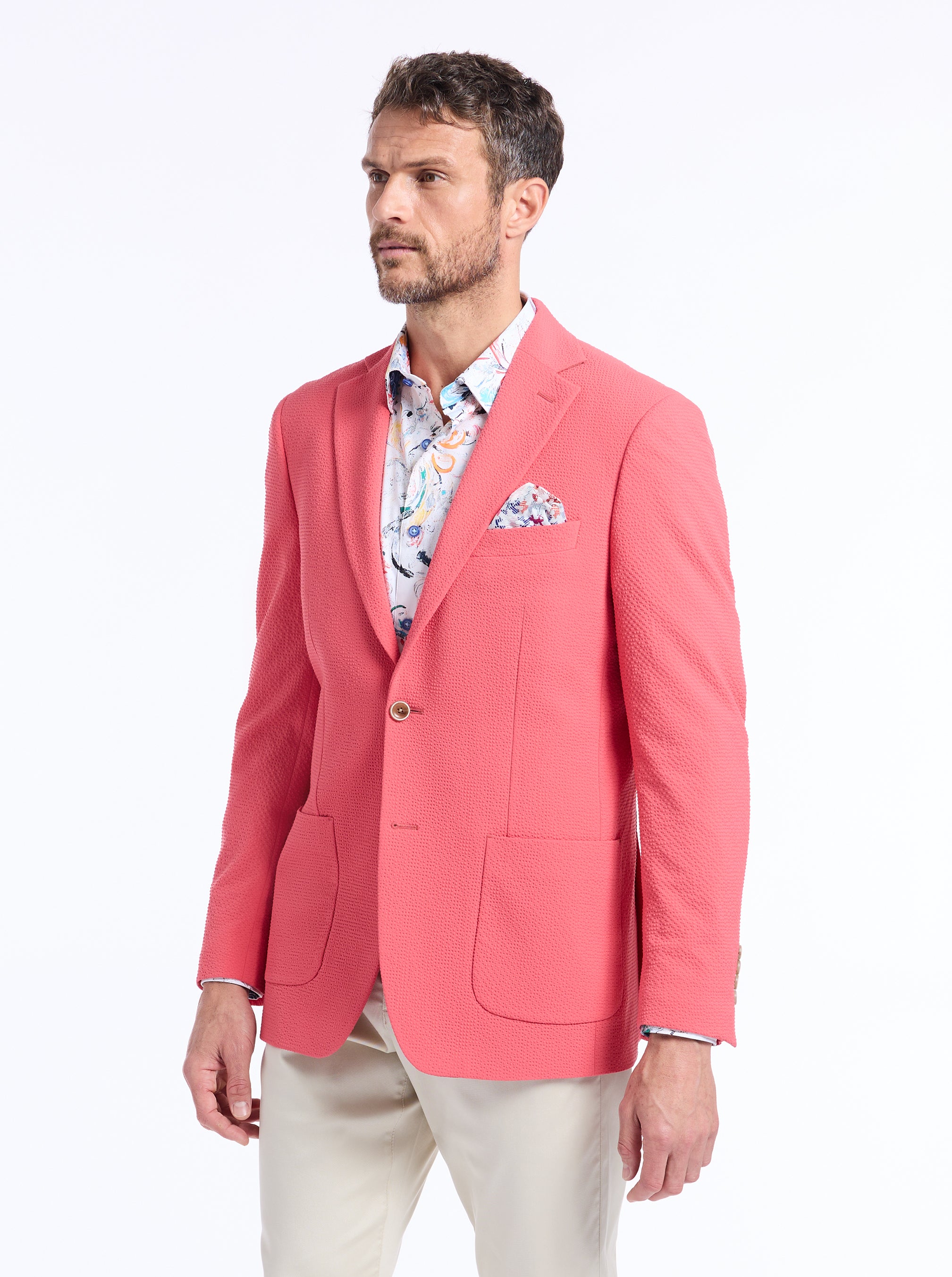 Man wearing a pink blazer over a patterned shirt on a white background