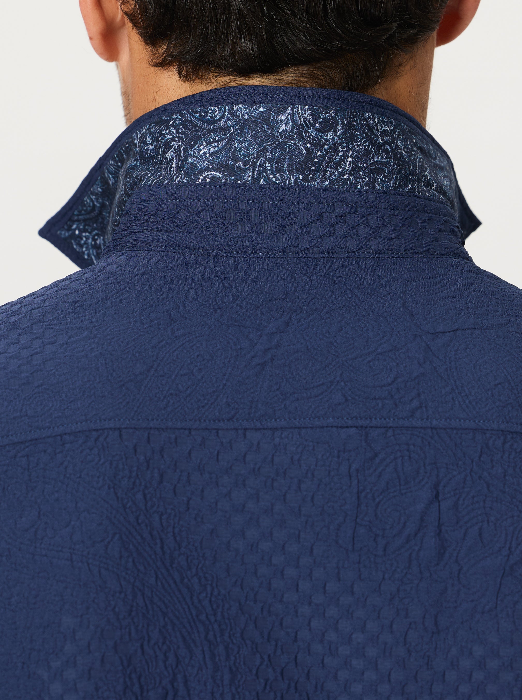 Close-up of a blue textured shirt with a patterned collar against a light background