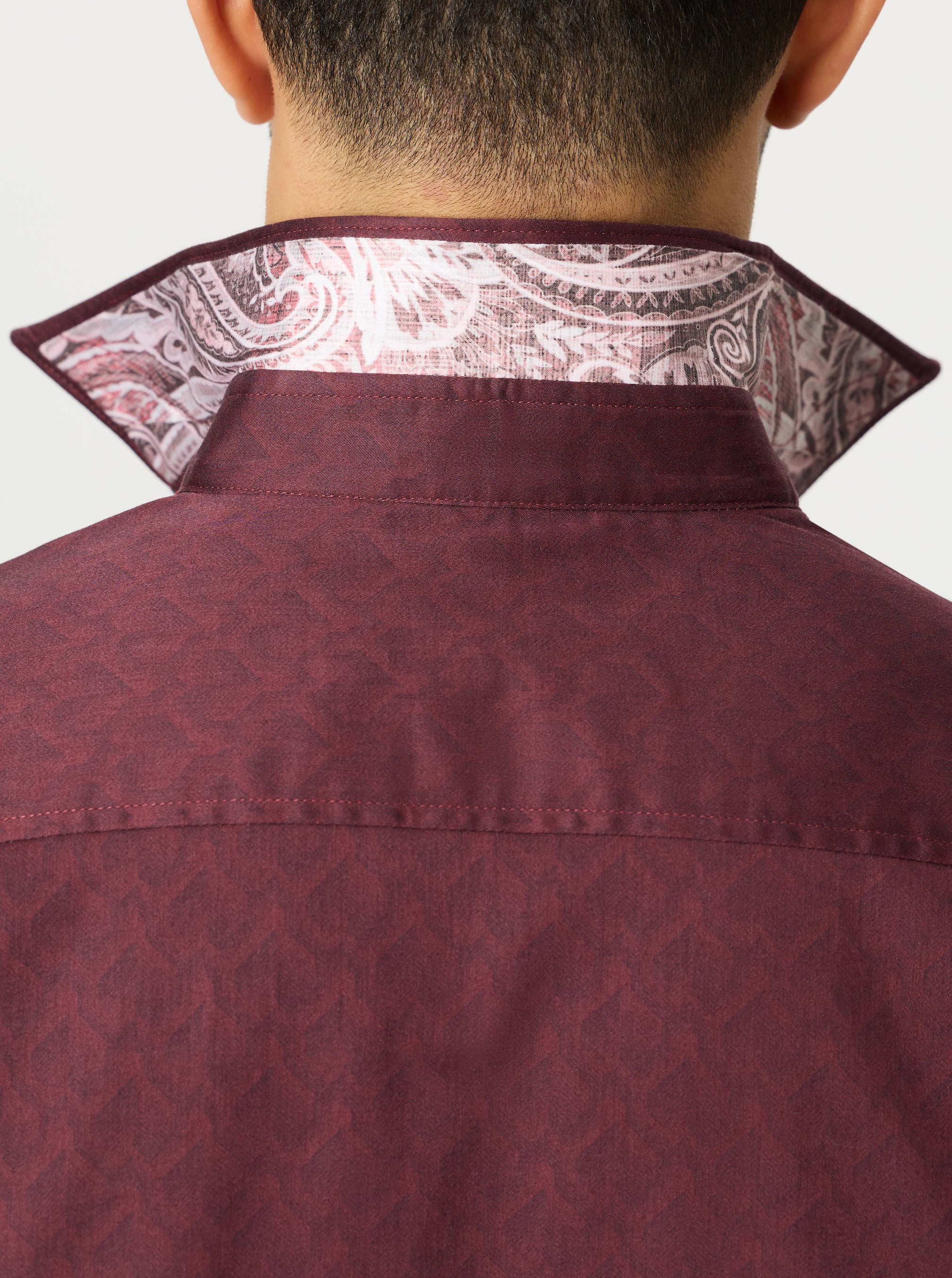 Close-up of a maroon shirt with a geometric pattern and contrast patterned collar against a light gray background