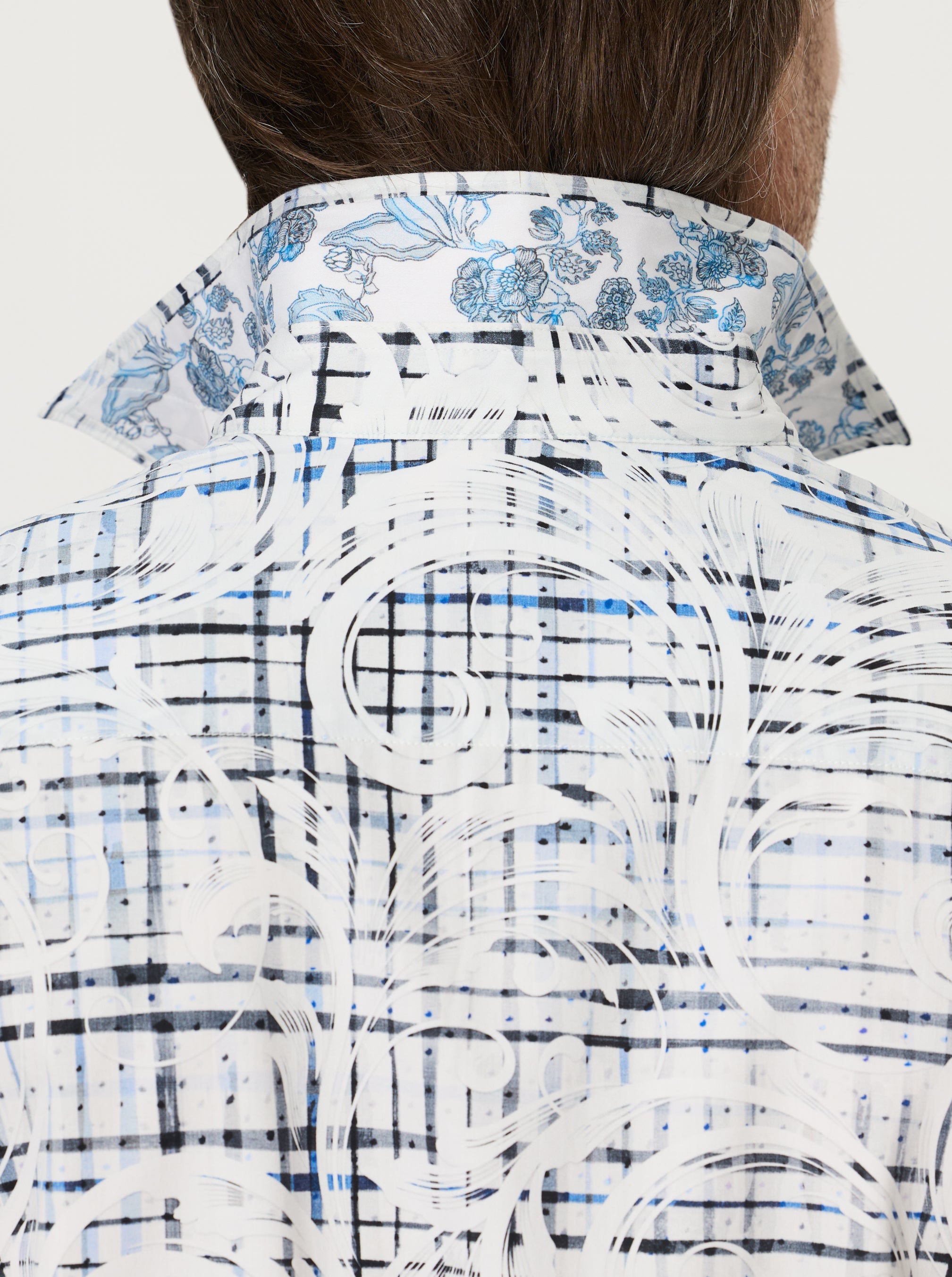 Close-up of a plaid and paisley patterned shirt with a visible brand logo on a white background