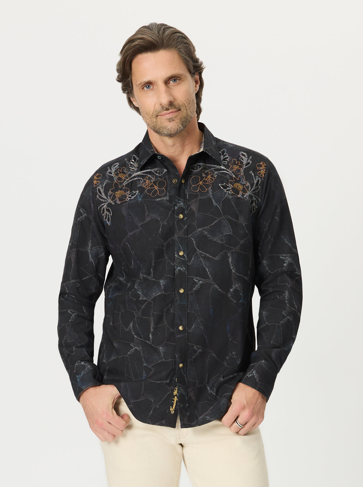 Man wearing a black patterned shirt with beige pants on a white background