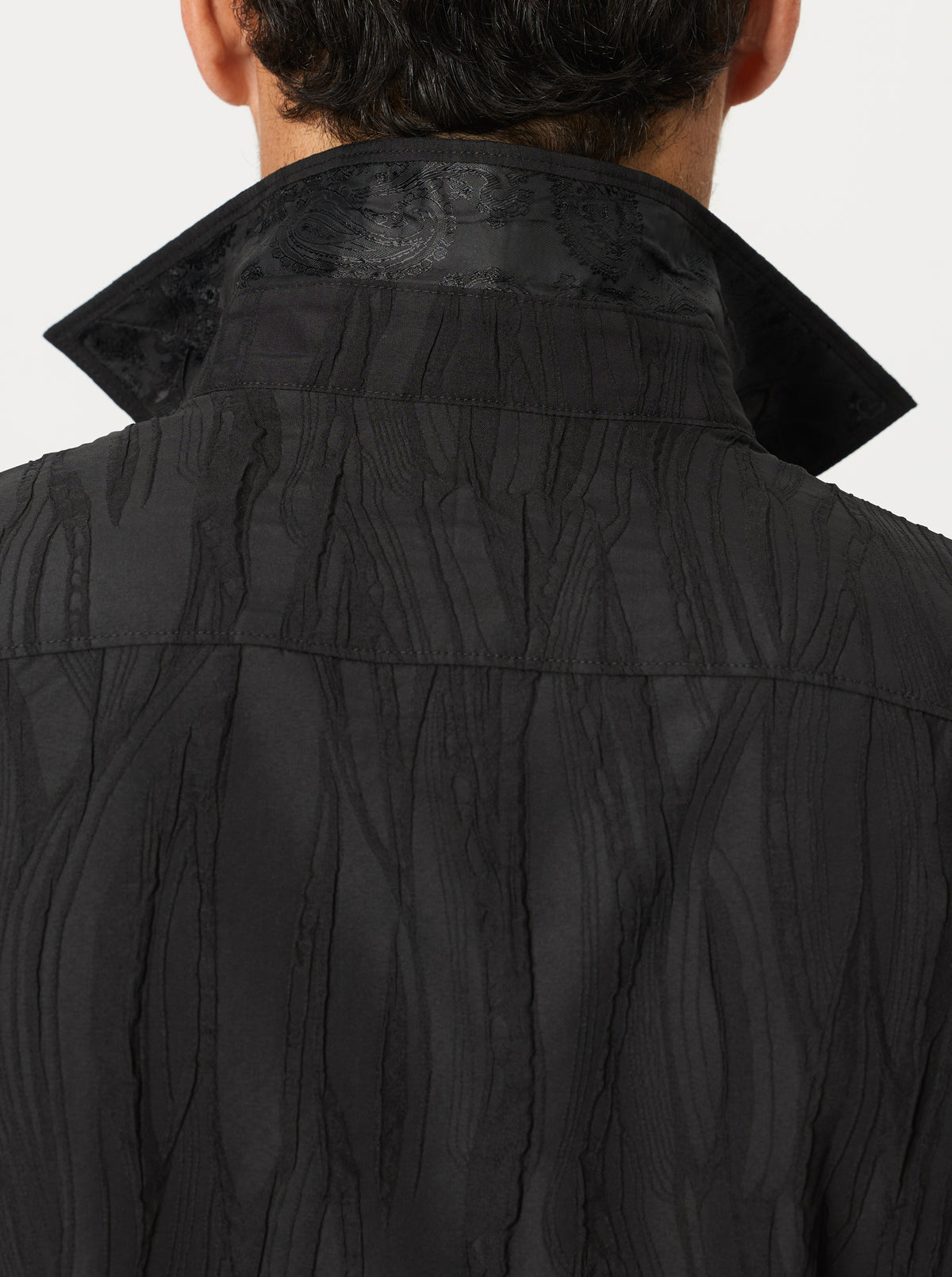 Close-up of a textured black jacquard shirt with a hood on a light gray background