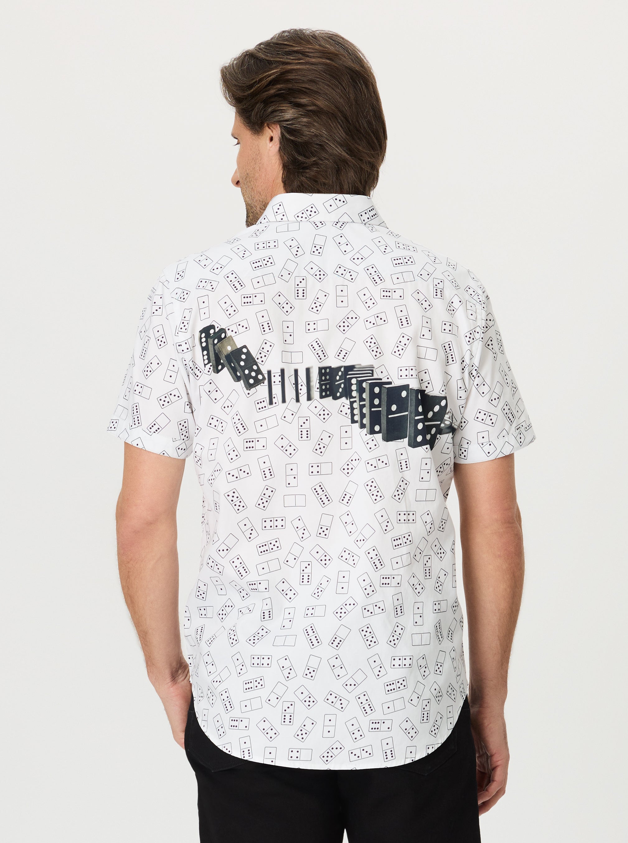 Person wearing a white shirt with black dominos patterns on a plain background