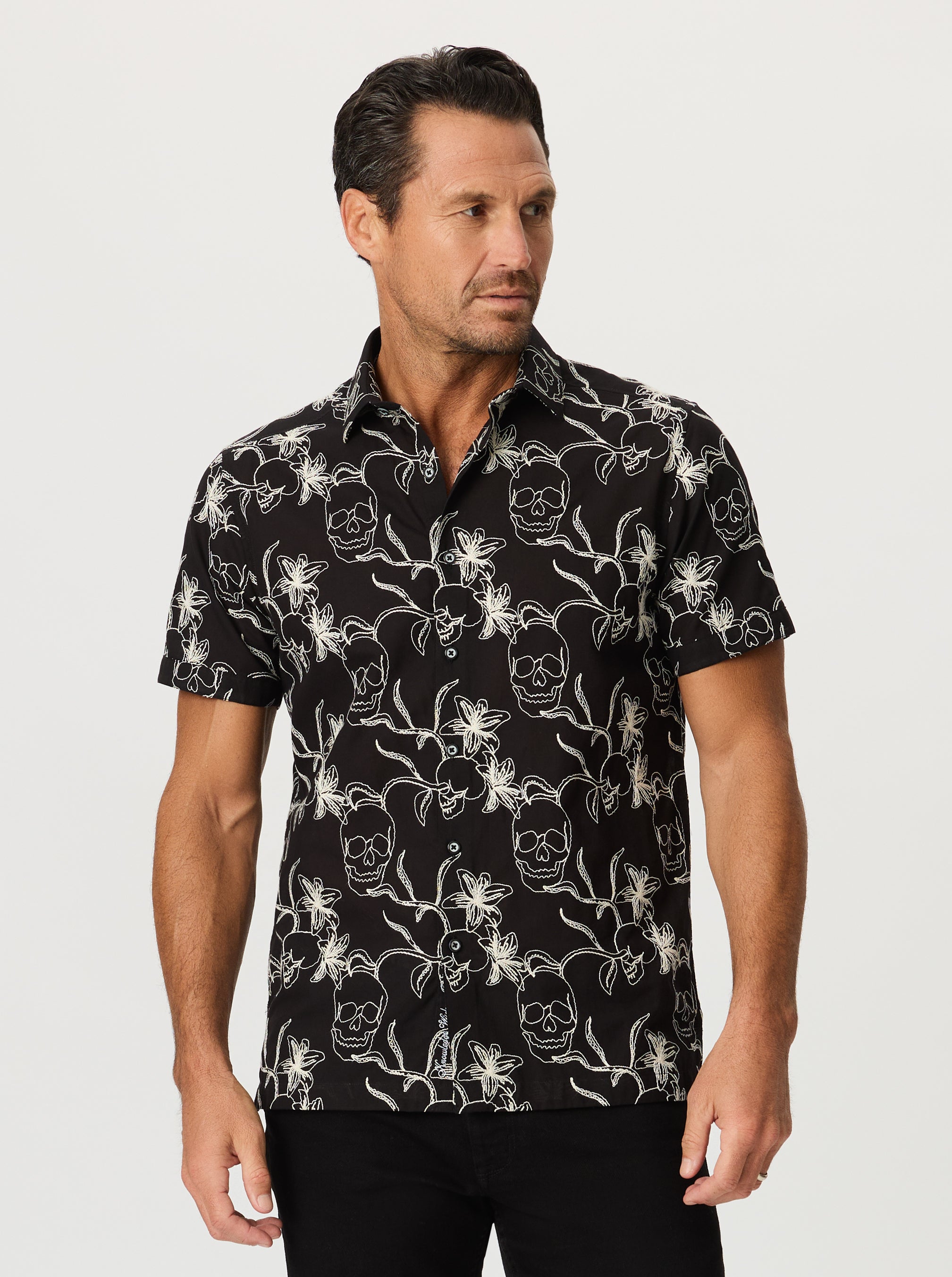Man wearing a black floral and skull patterned shirt against a white background