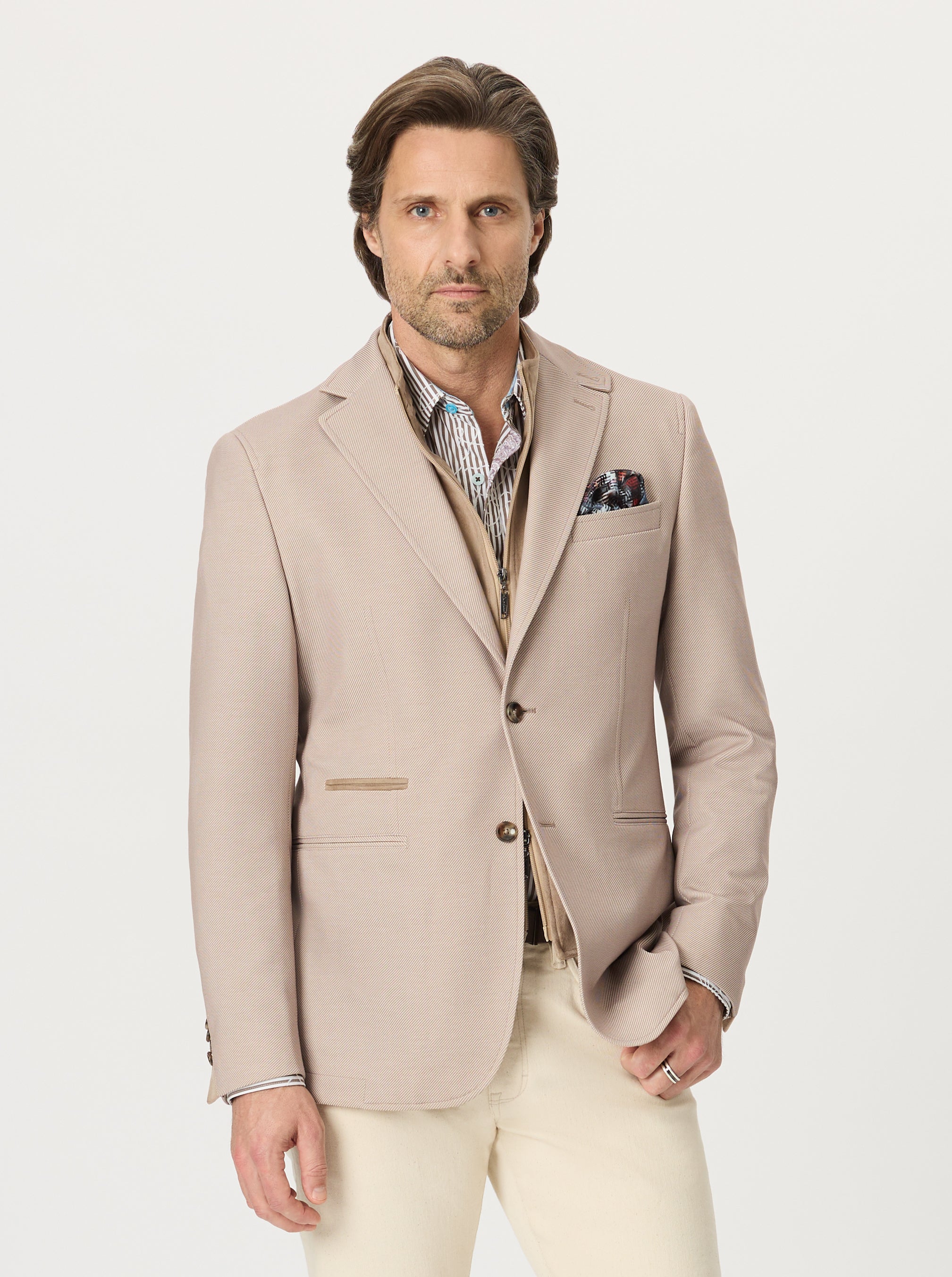 Man wearing a beige blazer over a patterned shirt with a white background