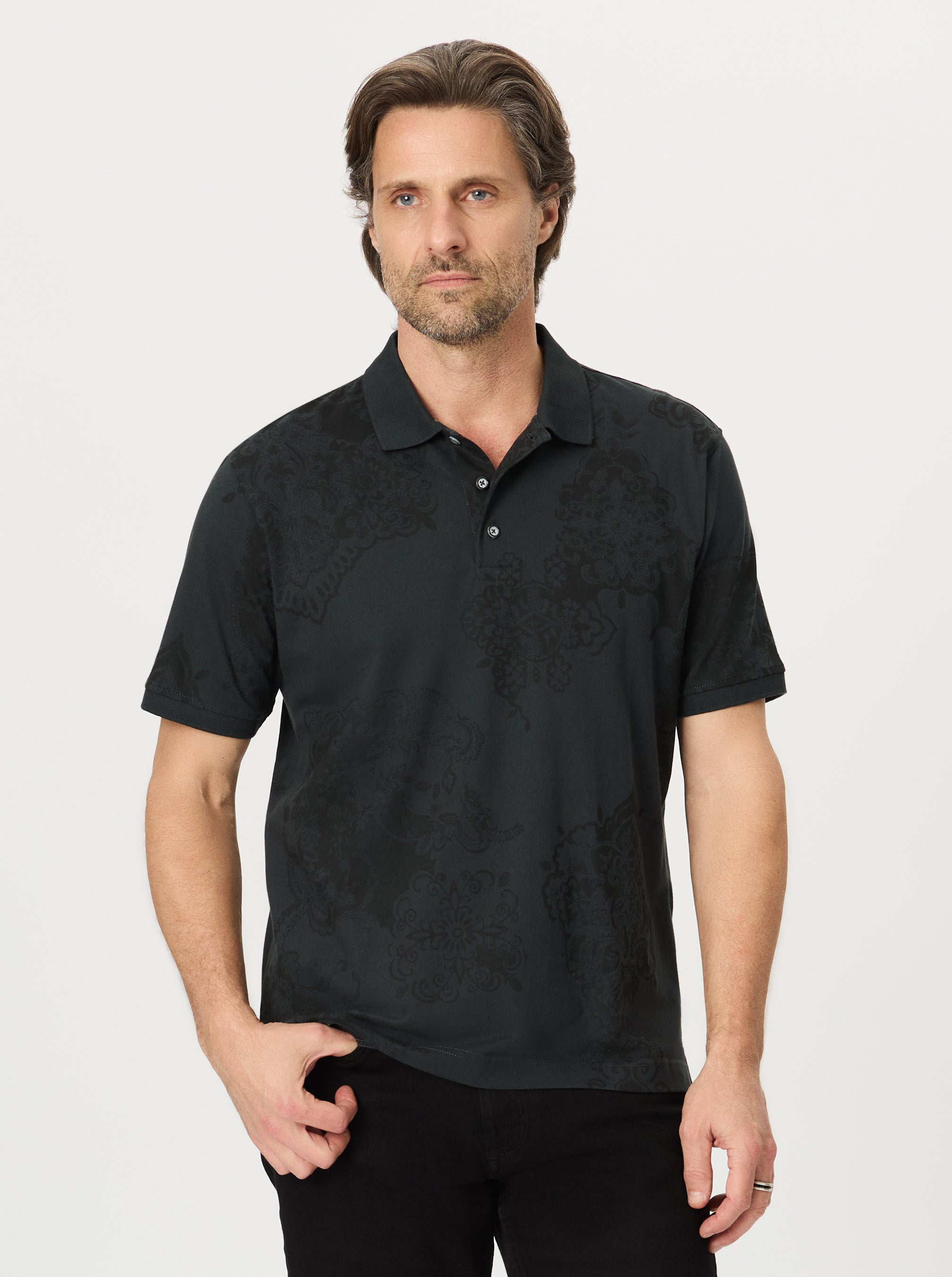 Man wearing a black paisley patterned polo shirt against a plain background