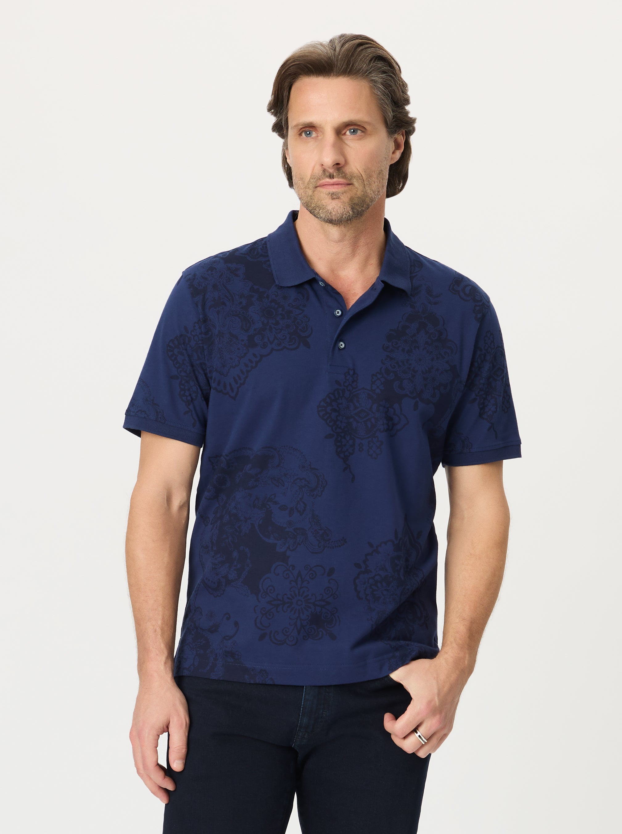 Man wearing a navy paisley patterned polo shirt on a light gray background