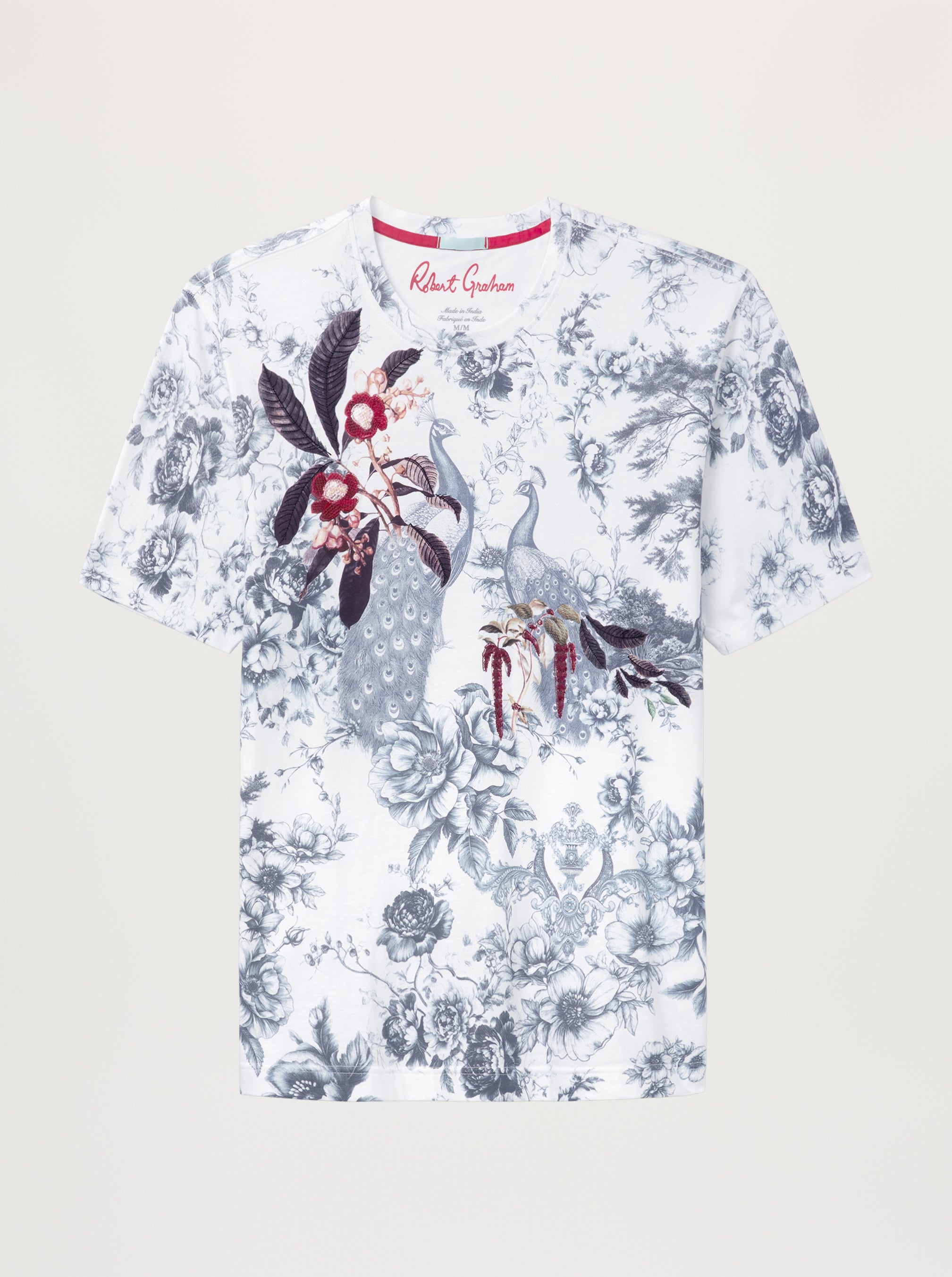 A short-sleeve crewneck t-shirt featuring a white base with a blue-gray toile floral print and a central graphic of a peacock with red and black accents.