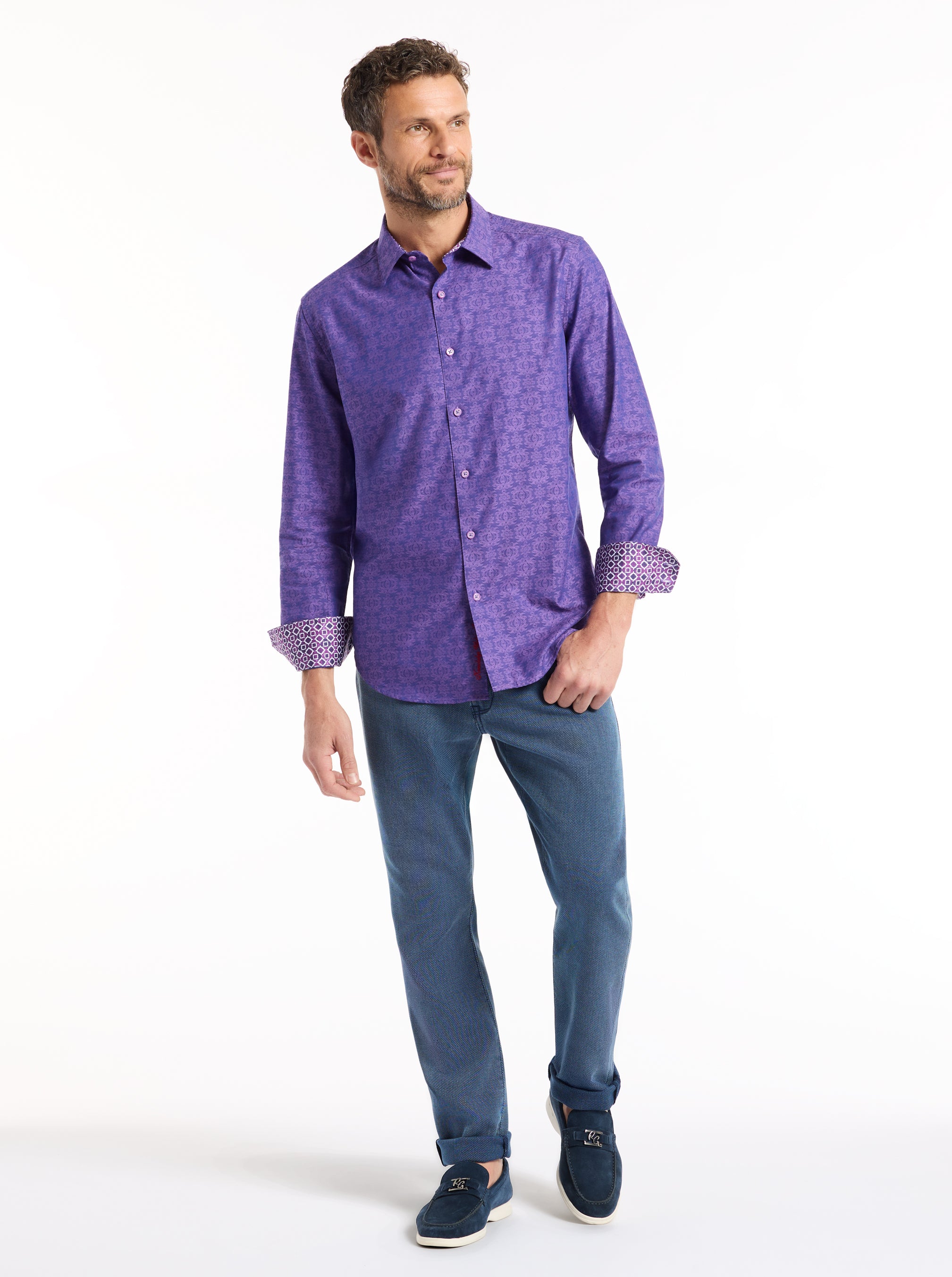 Man wearing a purple patterned shirt and blue jeans on a white background