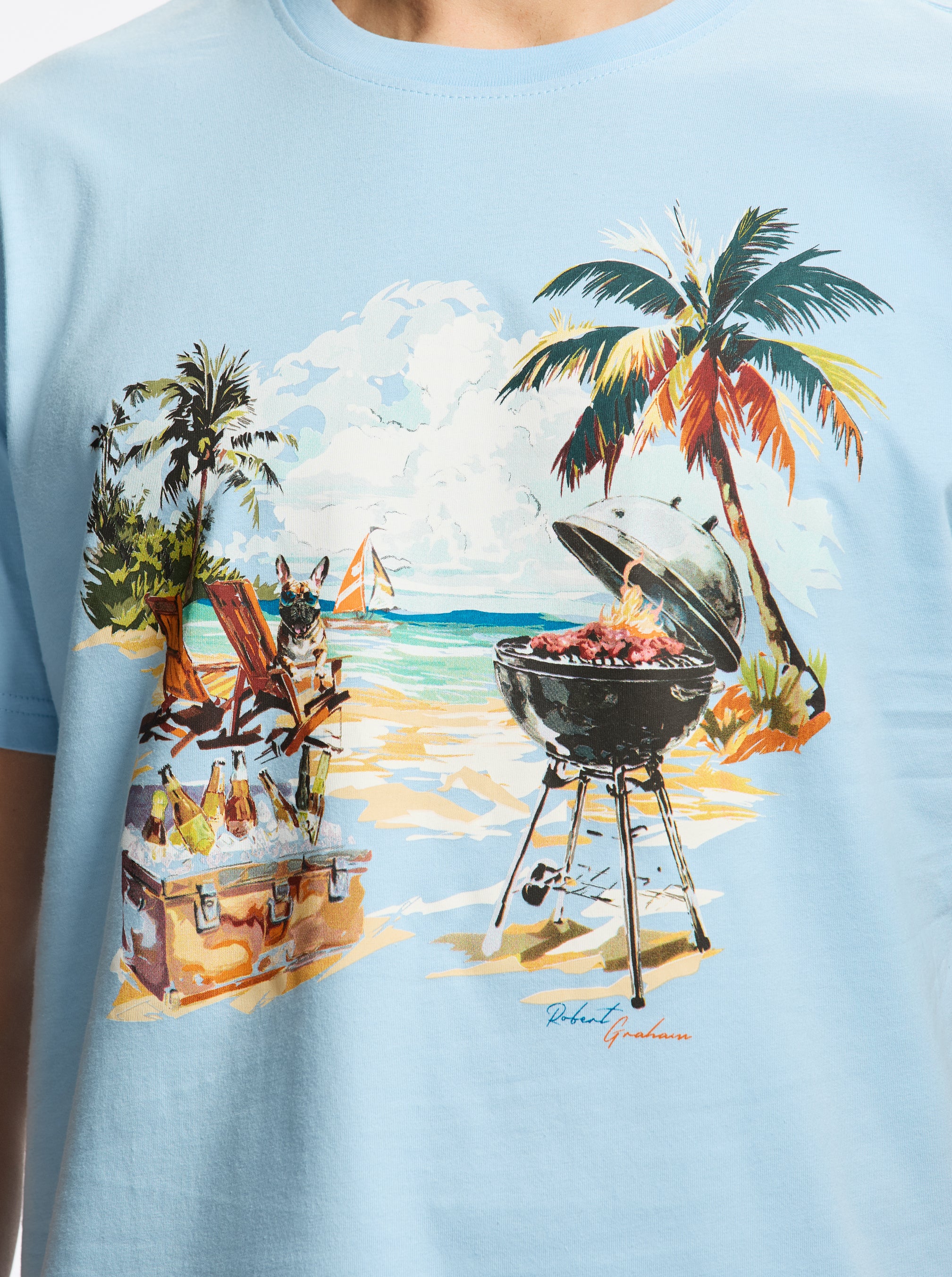 Light blue t-shirt with a beach scene graphic featuring a grill drinks, and palm trees.