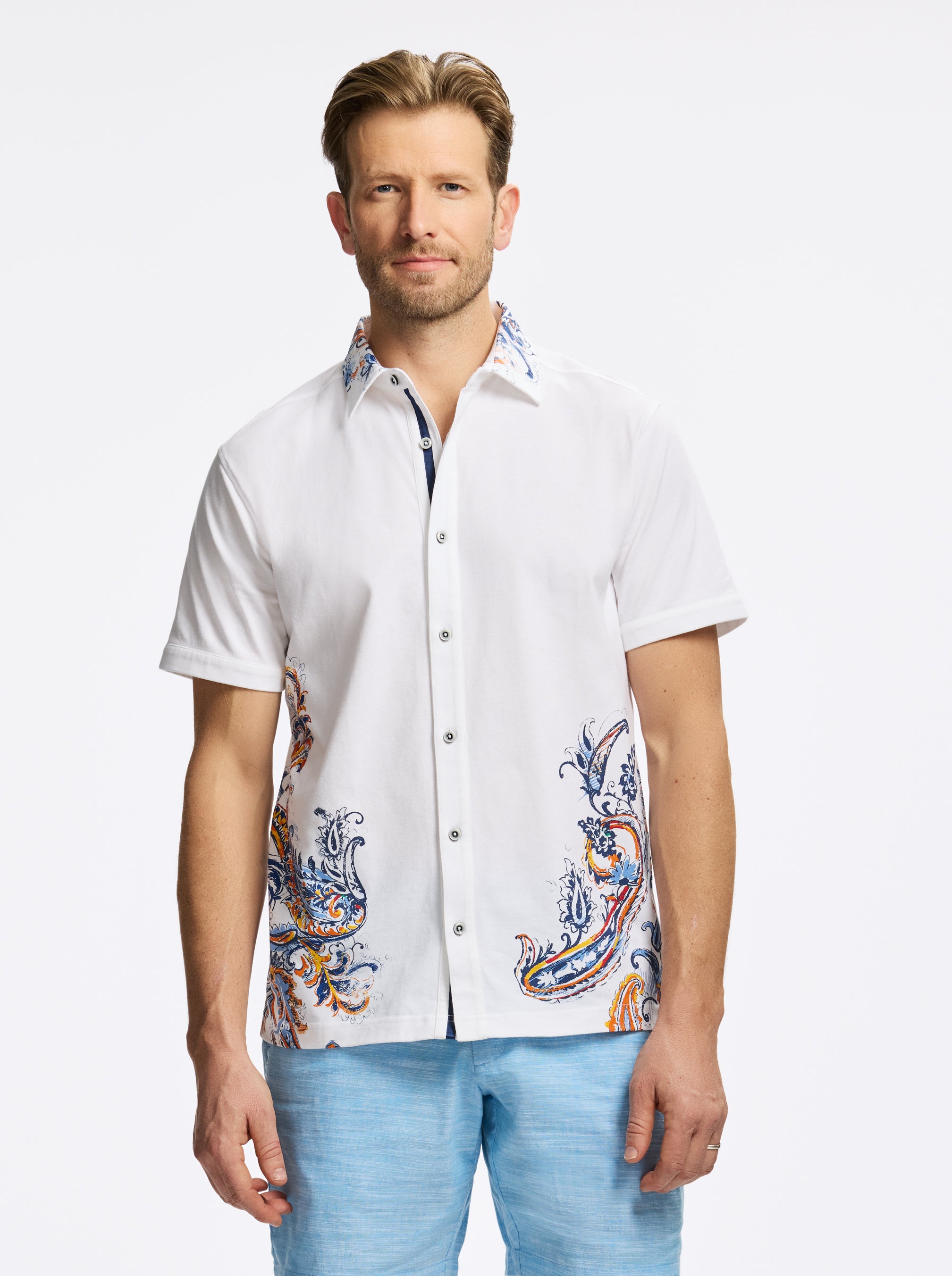 Man wearing a white short-sleeve shirt with colorful patterns and light blue pants on a white background