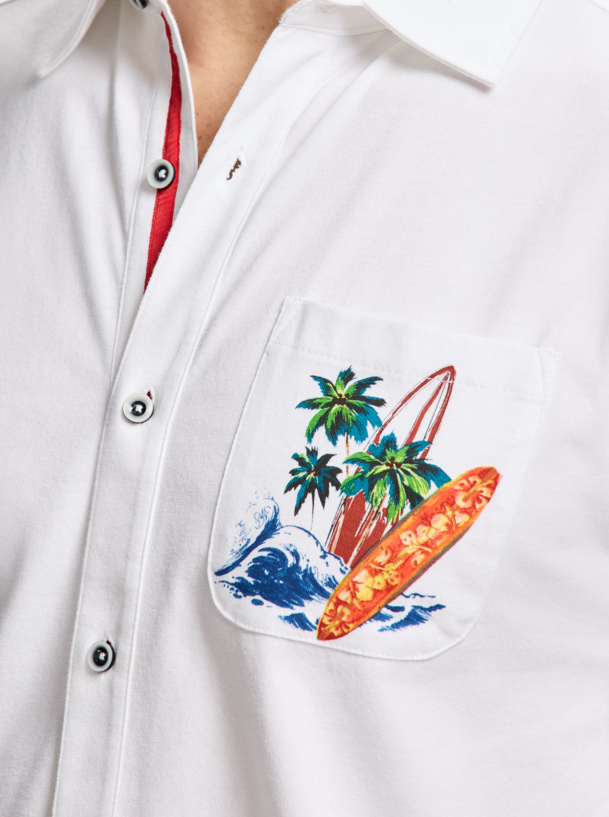 White shirt with a colorful pocket design featuring palm trees and surfboards.