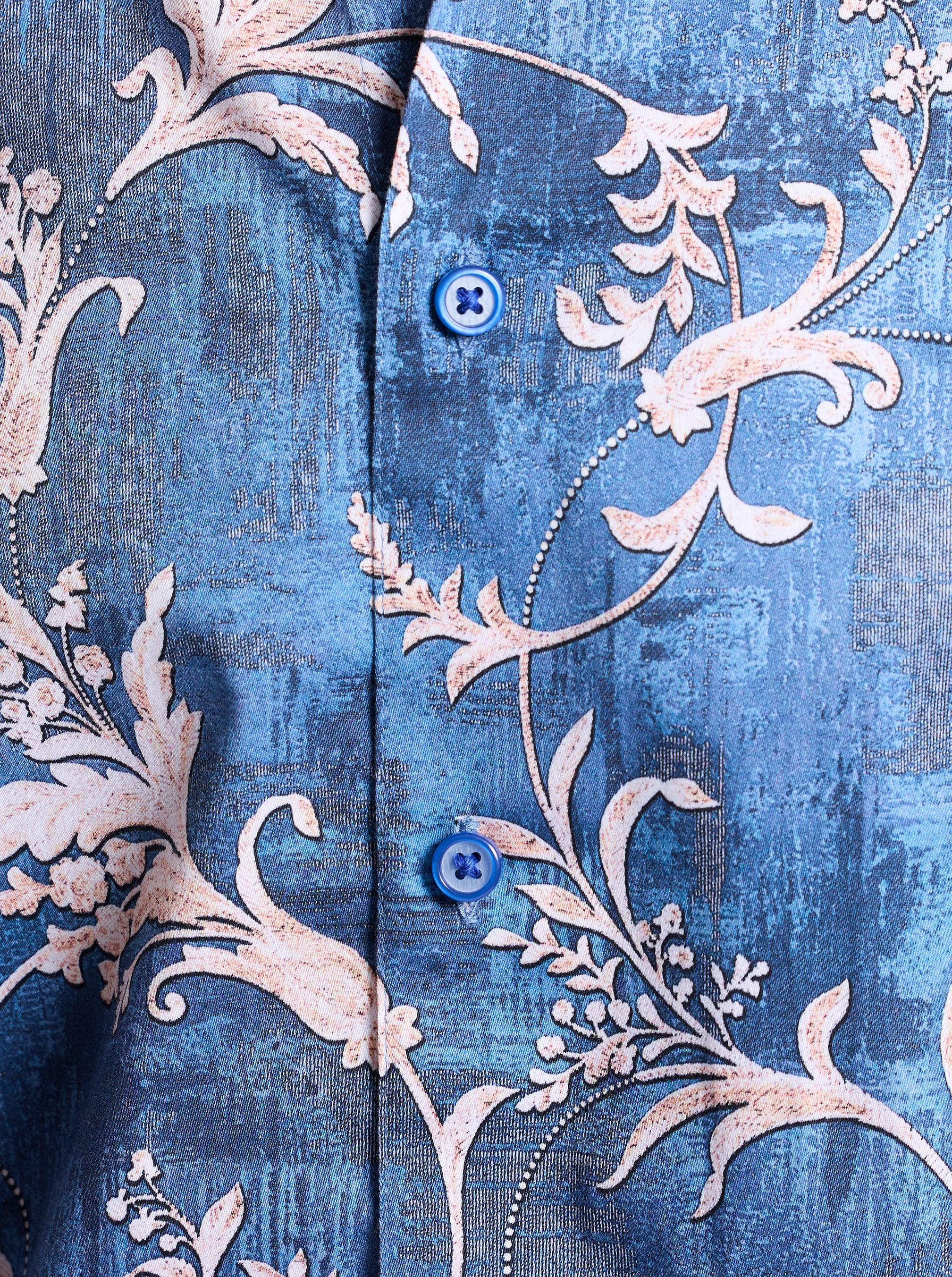 Close-up of a blue fabric with intricate white floral patterns and buttons.