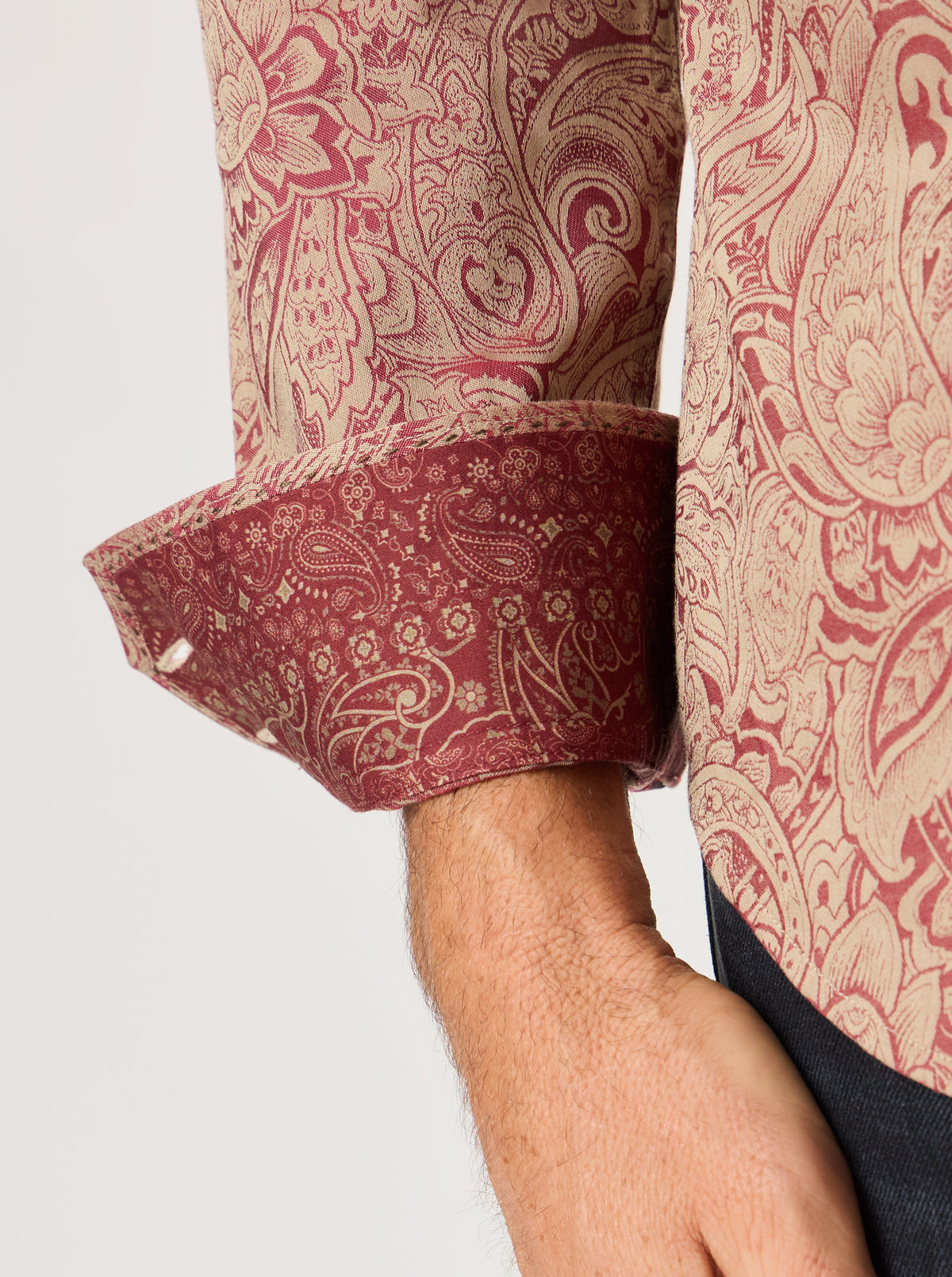 Close-up of a patterned shirt sleeve and cuff with a paisley print in dusty red and beige, worn by a model.