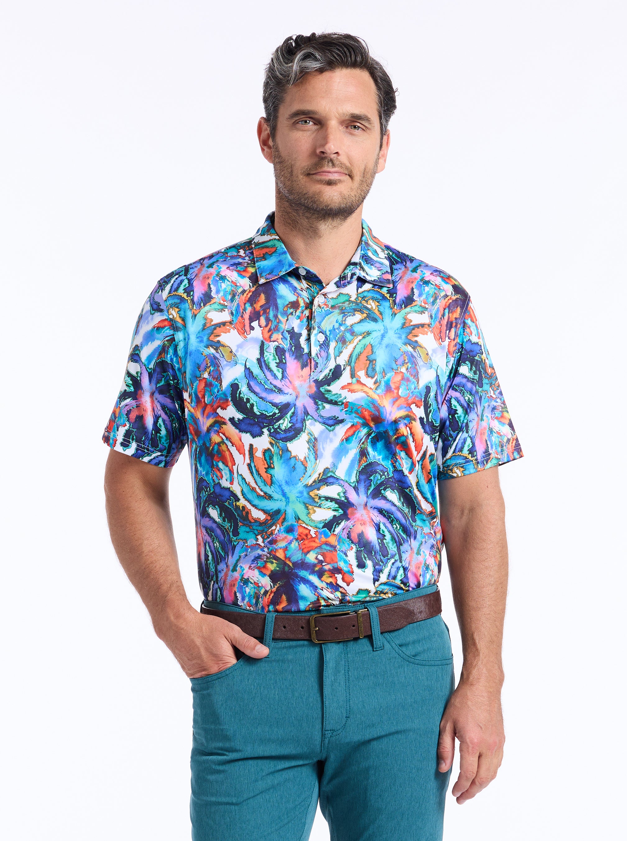 Man wearing a colorful palm tree patterned shirt and teal pants on a white background