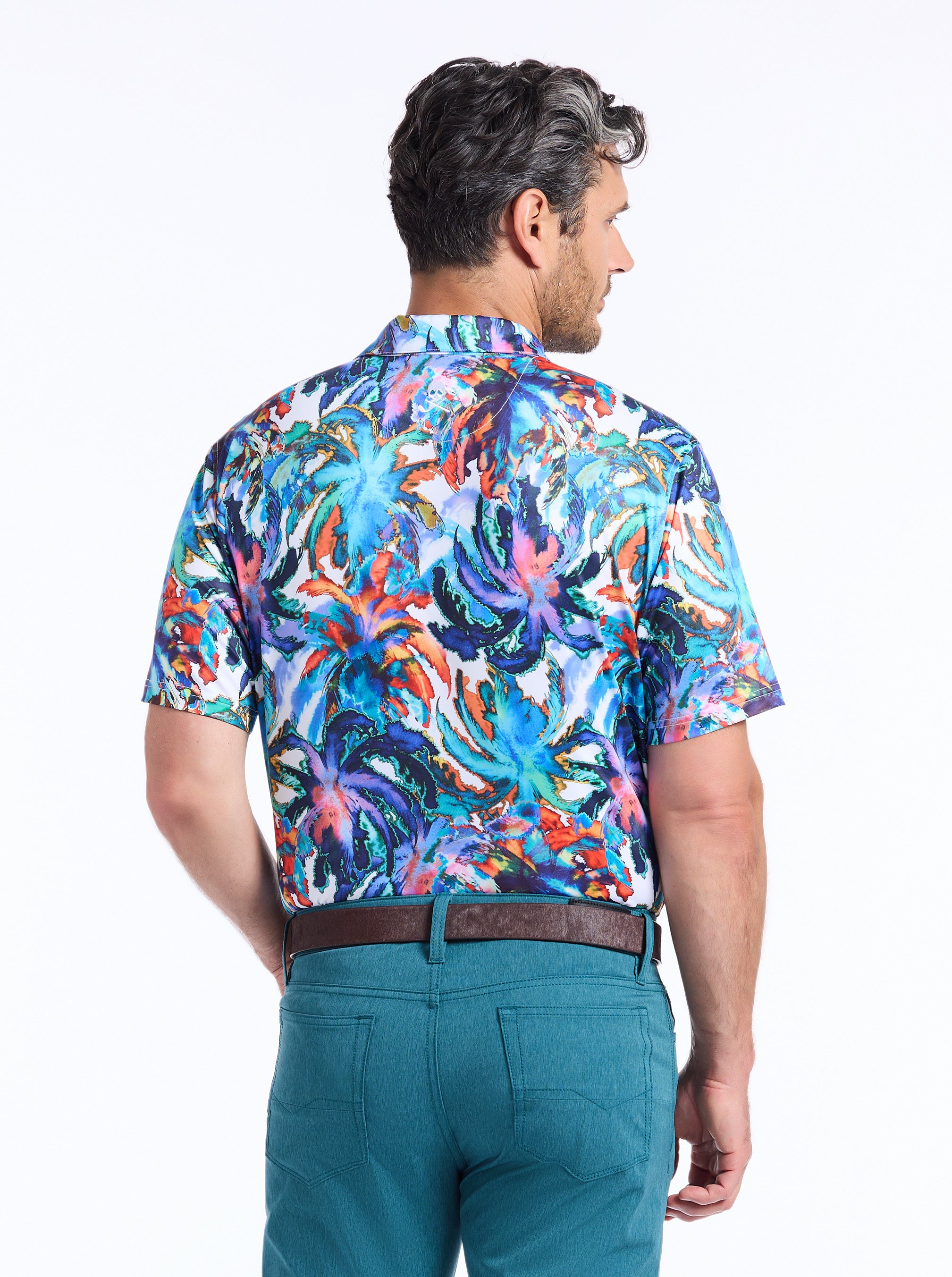 Man wearing a colorful patterned shirt and teal pants on a white background
