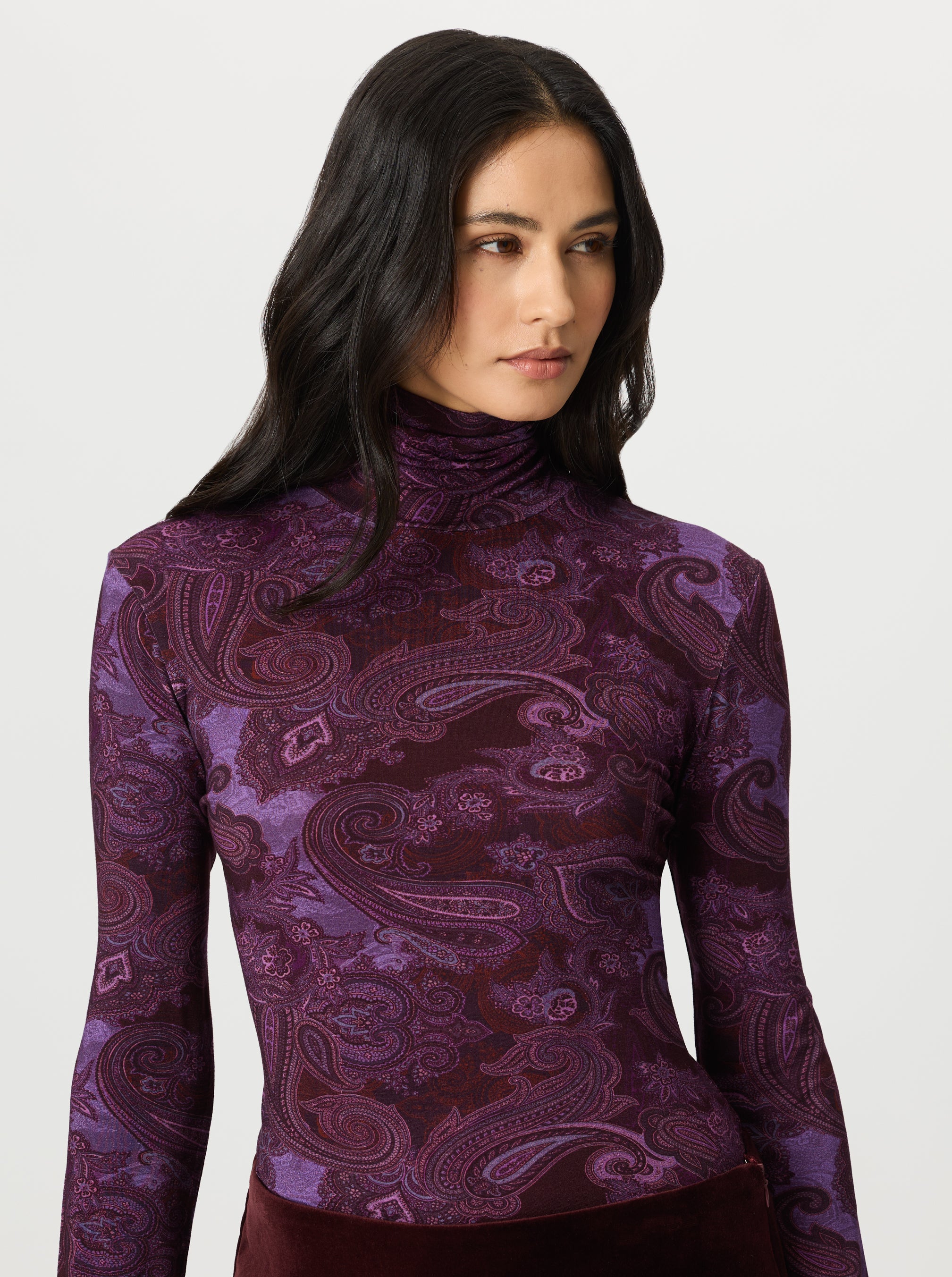 Woman wearing a purple paisley patterned turtleneck shirt on a white background